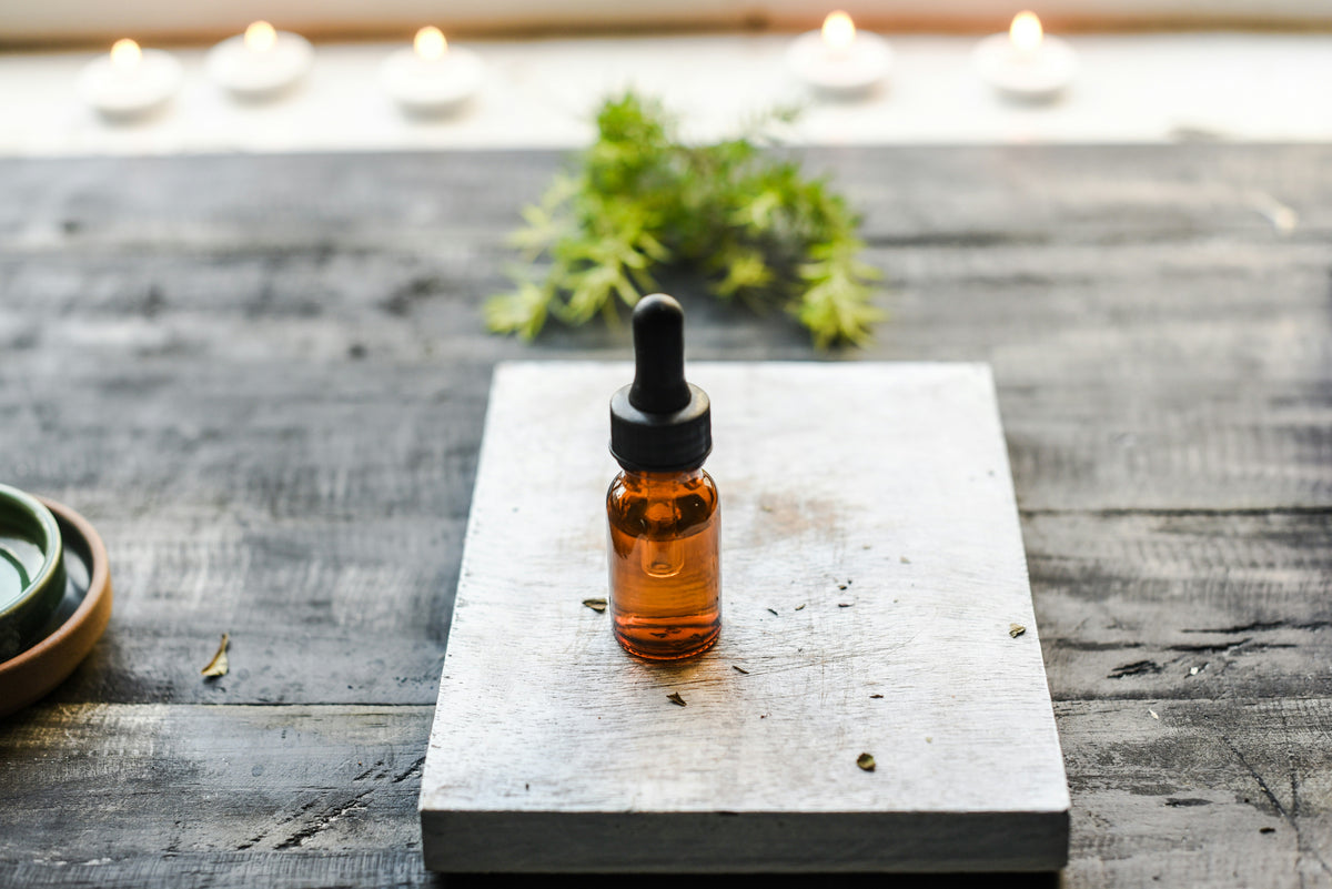 Essential oil dropper bottle with candles and greenery, calming wellness aromatherapy scene